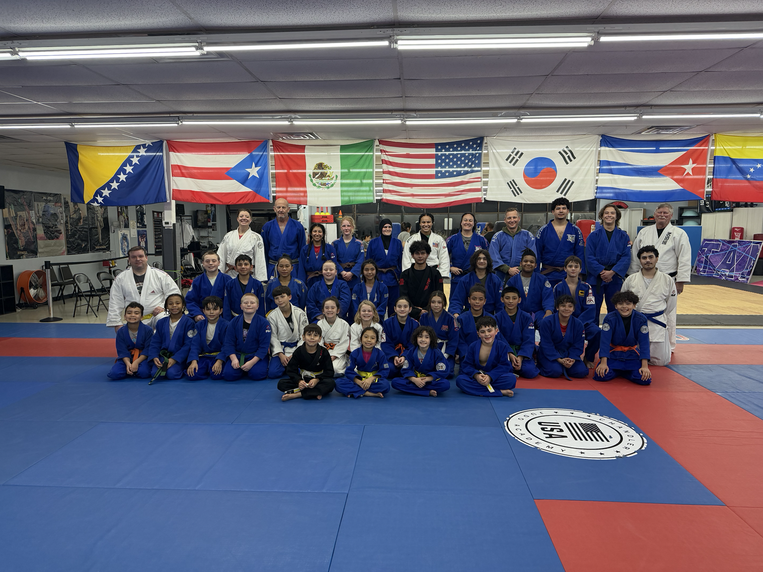 The full Chandler Judo Academy team posed on the mat with international flags in the background